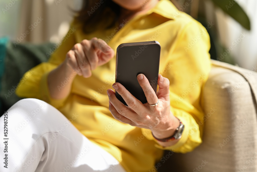 Cropped image of middle-aged old 60s woman touching a smartphone, using mobile app, chatting on internet, texting message, search ecommerce offers on cell phone technology device. Cropped image of middle-aged old 60s woman touching a smartphone, using mobile app, chatting on internet, texting message, search ecommerce offers on cell phone technology device.