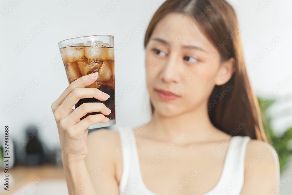 Avoid, limits sweet sugar, choose asian young woman, girl holding, looking at a glass of cold cola soft drink soda, sparkling water with ice by her hand. Health care, healthy diet lifestyle concept. Avoid, limits sweet sugar, choose asian young woman, girl holding, looking at a glass of cold cola soft drink soda, sparkling water with ice by her hand. Health care, healthy diet lifestyle concept.