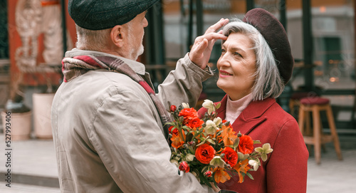 Elderly senior love couple. Old retired man woman together on romantic date.Aged husband wife walking on city street with flowers.Stylish elder hugging people pensioner in red coat.Happy family years