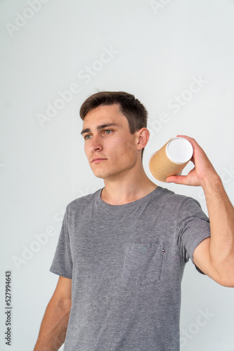 Young caucasian man in a t-shirt posing with a cup of coffee on a white background