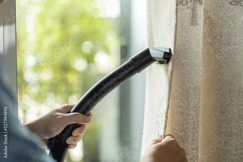 man dry cleaning curtain with vacuum cleaner. in living room at home.