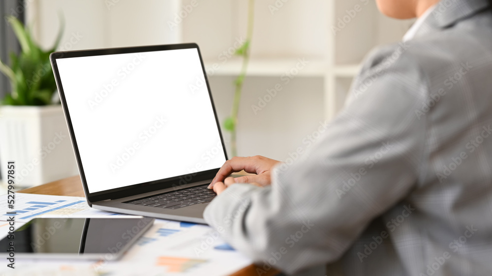 Cropped shot of businesswoman working with financial document and using laptop at her office desk Cropped shot of businesswoman working with financial document and using laptop at her office desk