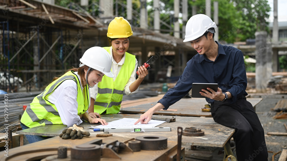Smiling civil engineer and architects are planning development details and inspecting industrial building construction site