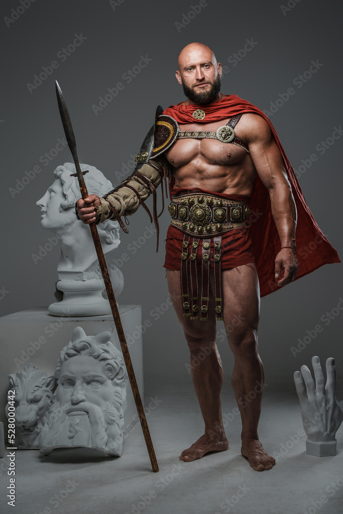 Portrait of greek gladiator from past holding spear posing around greek busts. Portrait of greek gladiator from past holding spear posing around greek busts.