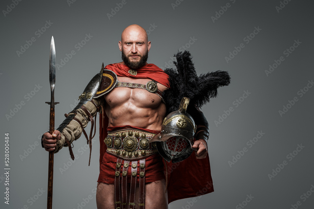 Naklejka premium Shot of antique roman warrior with muscular build holding helmet and spear.