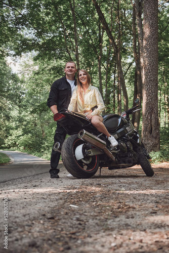 Young beautiful couple hugging, sitting on a motorcycle, travel together on a forest road