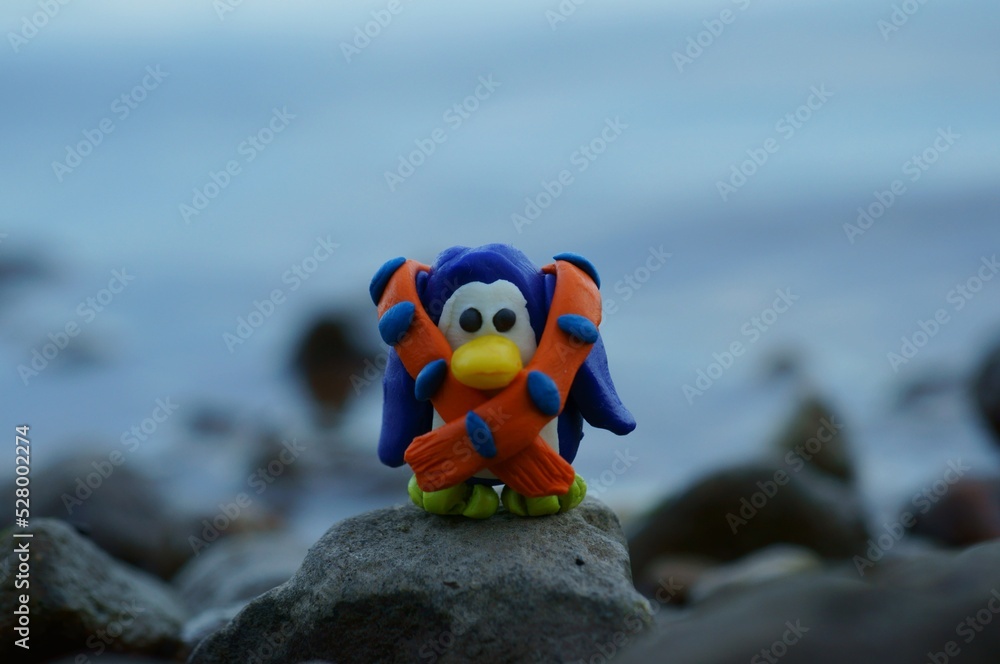 Obraz premium A toy penguin in a scarf on the background of the sea. Evening twilight. Beautiful toys.