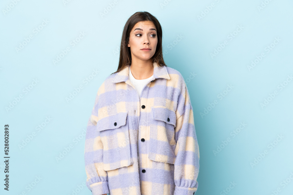 Young caucasian woman isolated on blue background making doubts gesture looking side Young caucasian woman isolated on blue background making doubts gesture looking side