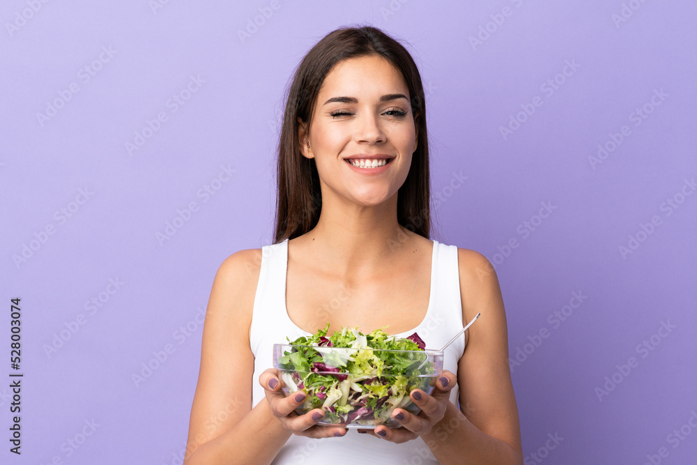 Young caucasian woman with salad isolated on purple background