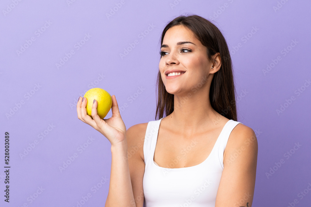 Young caucasian woman isolated on purple background with an apple and happy Young caucasian woman isolated on purple background with an apple and happy