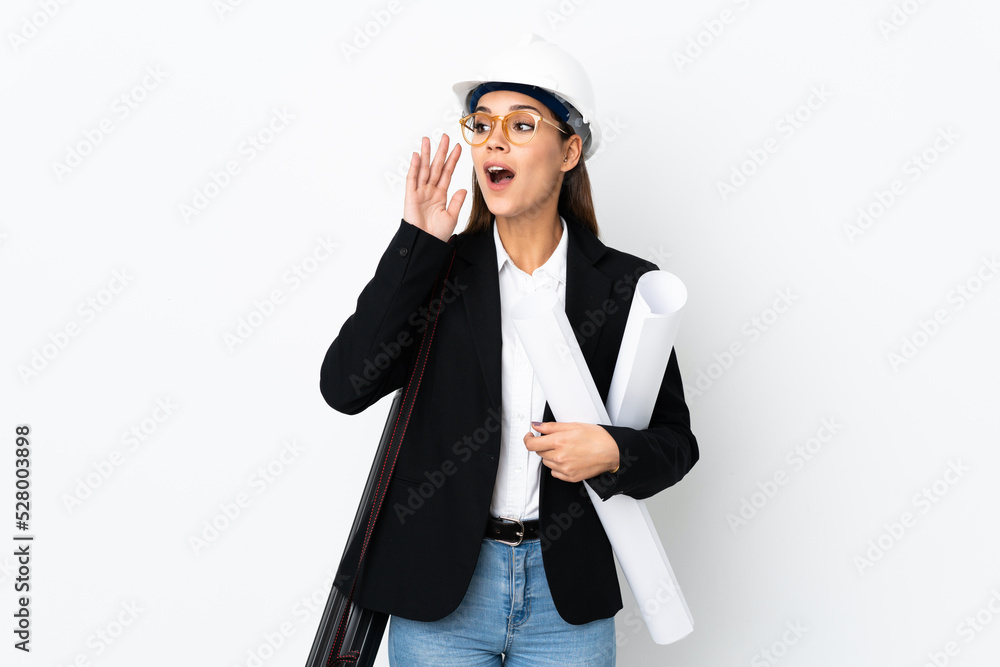 Young architect caucasian woman with helmet and holding blueprints over isolated background shouting with mouth wide open Young architect caucasian woman with helmet and holding blueprints over isolated background shouting with mouth wide open
