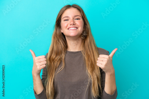 Young blonde woman isolated on blue background with thumbs up gesture and smiling