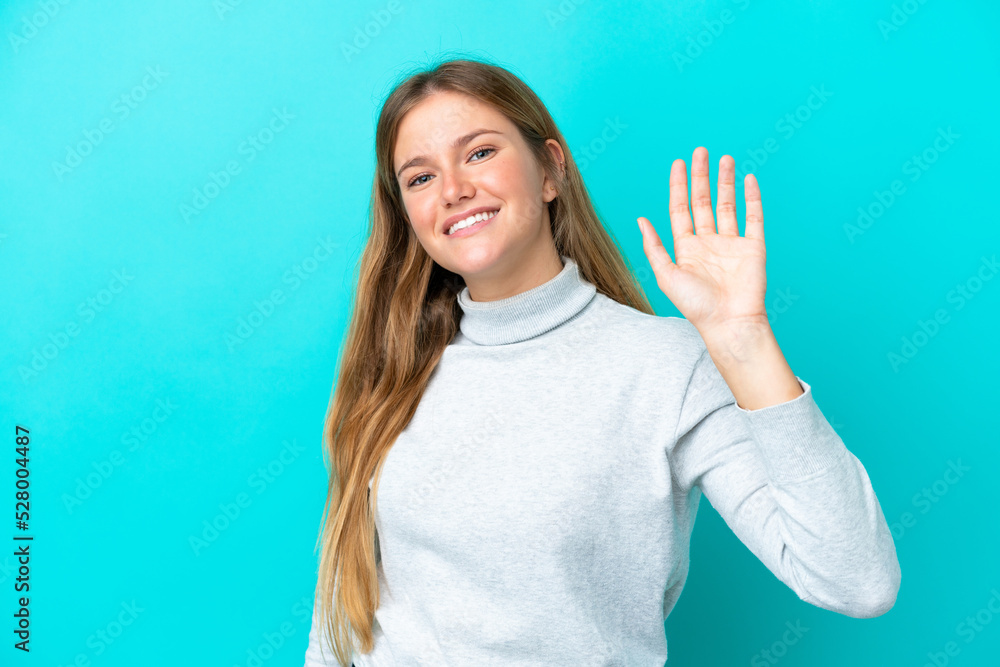 Fototapeta premium Young blonde woman isolated on blue background saluting with hand with happy expression