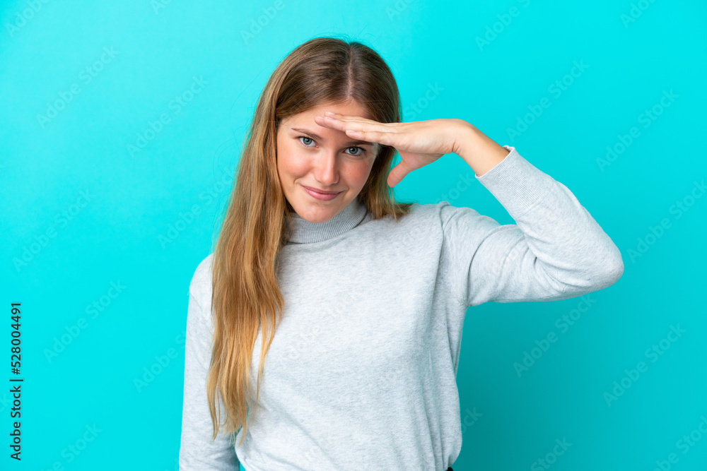 Young blonde woman isolated on blue background looking far away with hand to look something Young blonde woman isolated on blue background looking far away with hand to look something