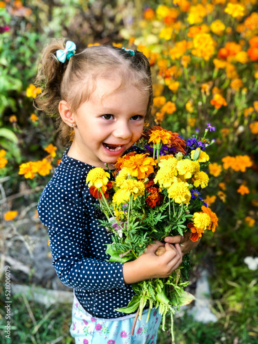 A little girl of European appearance poses with a huge bouquet of autumn flowers. Smiling child. The concept of a happy childhood