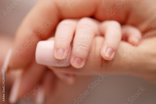 Close-up of a baby's small hand with tiny fingers and arm of mother on a white background. Newborn baby holding the finger of parents after birth The bond between mother and child Happy family concept © Vad-Len
