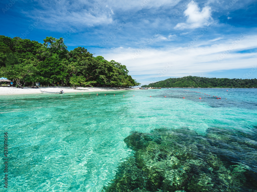 Scenic view of Koh Dong Island white sand beach and crystal clear turquoise sea water with coral reef against summer blue sky. Near Koh Lipe Island, Tarutao National Marine Park, Satun, Thailand.