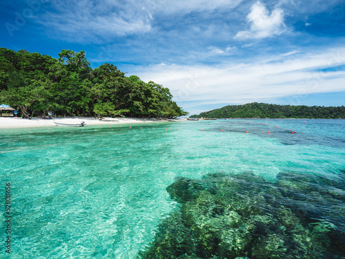 Scenic view of Koh Dong Island white sand beach and crystal clear turquoise sea water with coral reef against summer blue sky. Near Koh Lipe Island, Tarutao National Marine Park, Satun, Thailand.