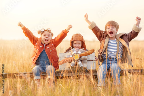 Little girl and boys is playing plane. Happy  funy children imagines himself an aircraft pilot and plays in a aviator costume in an open-air field against a blue sky on a summer day.  Games  dreams ab