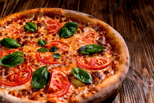Delicious fragrant pizza with mozzarella, tomatoes and basil with tomato sauce on woden background