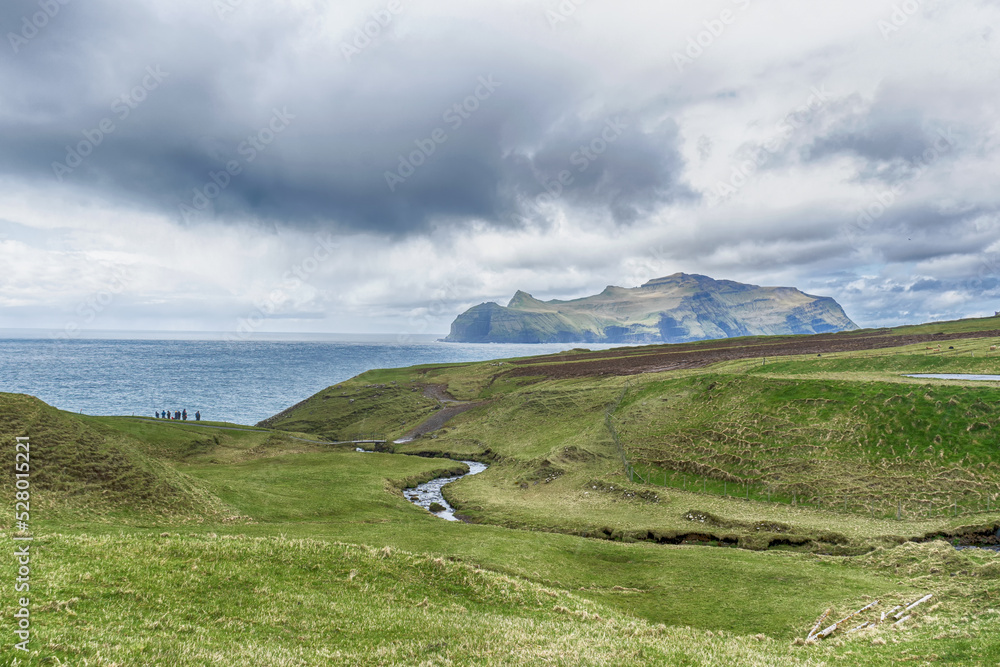 Fototapeta premium A group of people on the seashore. Beautiful island, beautiful mountains, and beautiful clouds in the blue sky. Faroe Islands. Denmark. Europe. Landscapes.