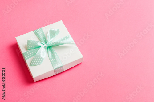 wrapped Christmas or other holiday handmade present in white paper with green ribbon on colored background. Present box, decoration of gift on colored table, top view with copy space © sosiukin