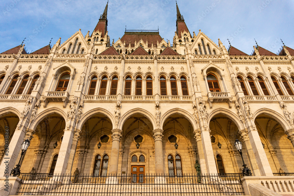 The Hungarian Parliament building. View of the main facade and south entrance during golden hour. Situated on Kossuth Square in the Pest side of Budapest, on the eastern bank of the Danube.