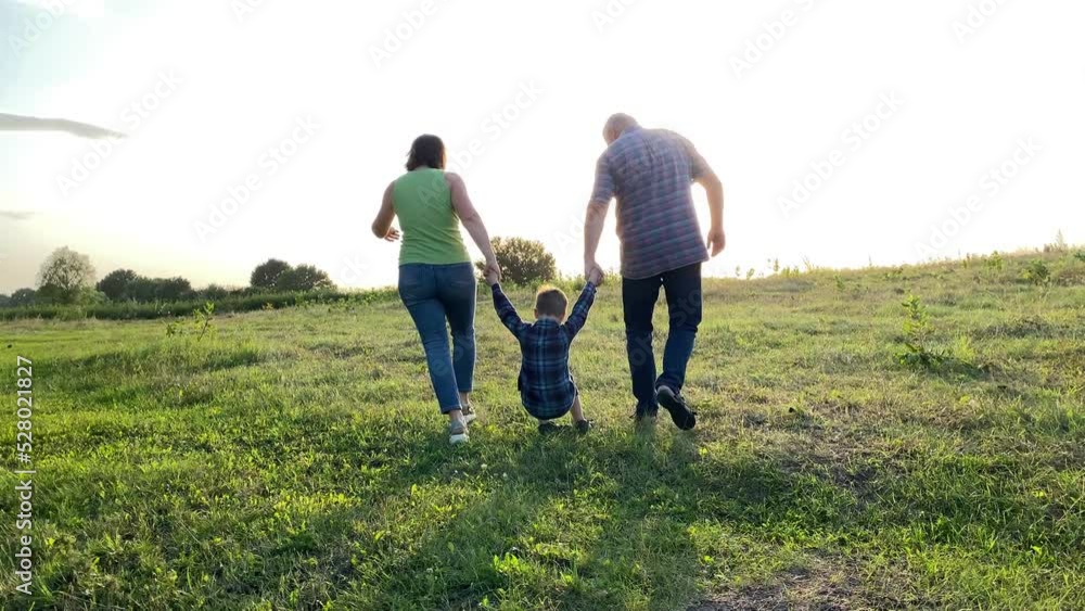 Silhouette of family with one child walking into sunset at meadow. Happy family spending time together outdoors. Little boy going near parents hand in hand, jumping in gold lights of summer sun Silhouette of family with one child walking into sunset at meadow. Happy family spending time together outdoors. Little boy going near parents hand in hand, jumping in gold lights of summer sun