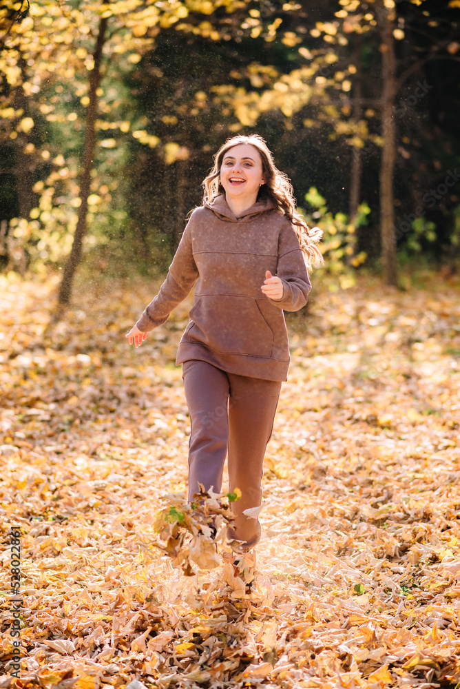 Young woman in hoodie sweater kicks up leaves in autumn park. Sunny weather. Fall season. Young woman in hoodie sweater kicks up leaves in autumn park. Sunny weather. Fall season.