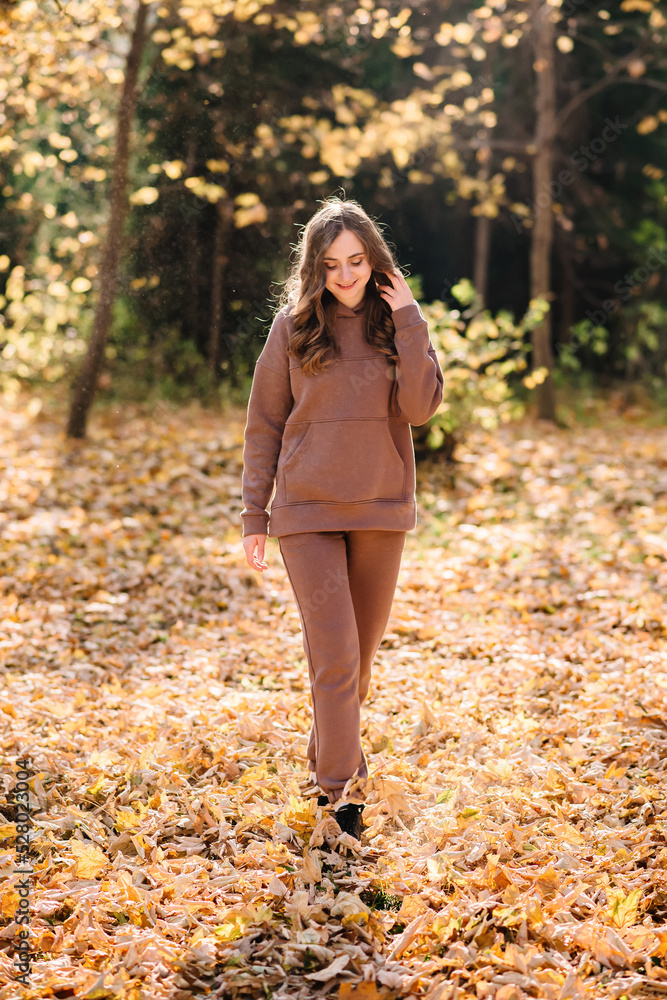Young woman in hoodie sweater walking in autumn park. Sunny weather. Fall season. Young woman in hoodie sweater walking in autumn park. Sunny weather. Fall season.