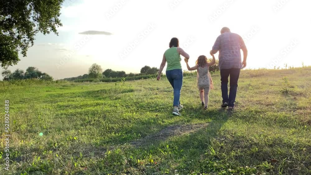 Silhouette of family with one child walking into sunset at meadow. Happy family spending time together outdoors. Little girl going near parents hand in hand, jumping in gold lights of summer sun Silhouette of family with one child walking into sunset at meadow. Happy family spending time together outdoors. Little girl going near parents hand in hand, jumping in gold lights of summer sun