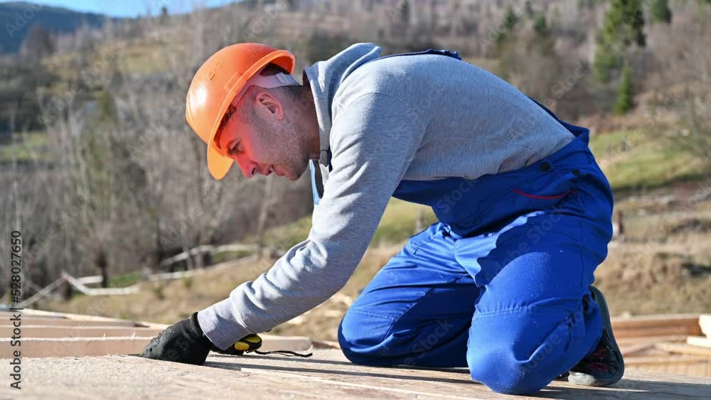 Man worker building wooden frame house. Carpenter using tape measure for measuring OSB sheet on rooftop. Carpentry concept. Man worker building wooden frame house. Carpenter using tape measure for measuring OSB sheet on rooftop. Carpentry concept.