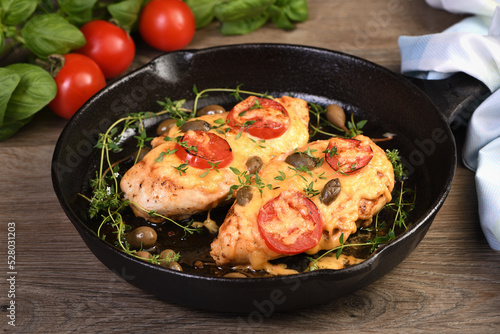 Tender chicken breast baked with tomatoes, capers, herbs under cheese crust in a frying pan