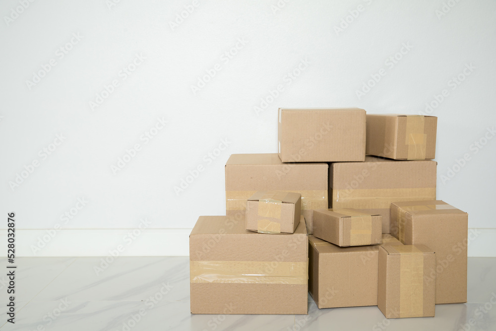 Stack of cardboard boxes for moving, Empty room with a white wall and cardboard boxes with unbranded barcode on the floor. Delivery of goods, shopping. Cardboard boxes on gray wall background. Stack of cardboard boxes for moving, Empty room with a white wall and cardboard boxes with unbranded barcode on the floor. Delivery of goods, shopping. Cardboard boxes on gray wall background.