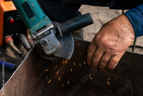 Man working with grinder saw, close up view on tool. Electric saw and hands of worker with sparks.