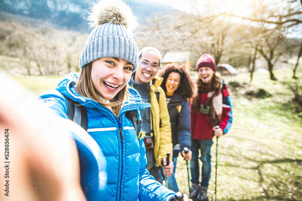 Happy group of friends with backpacks hiking in the mountains - Multiracial young people taking selfie hanging outside in weekend excursion trip - Sport and leisure lifestyle concept