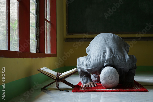 Portrait of Muslim man Sujud or prostration in a Sajdah with Quran and tasbih beside
