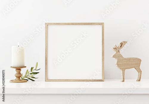 Brown square frame mockup in white interior with simple minimal Christmas decoration, candle and wooden deer. 3D rendering, illustration.