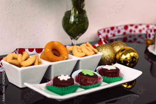 Rosquinhas com sequilhos e doces de chocolate na mesa posta com flores e bolas de natal