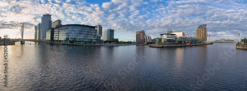 Panoramic view of several buildings in the city of Manchester, reflected in the calm waters of the central bay, and clouds at sunset.