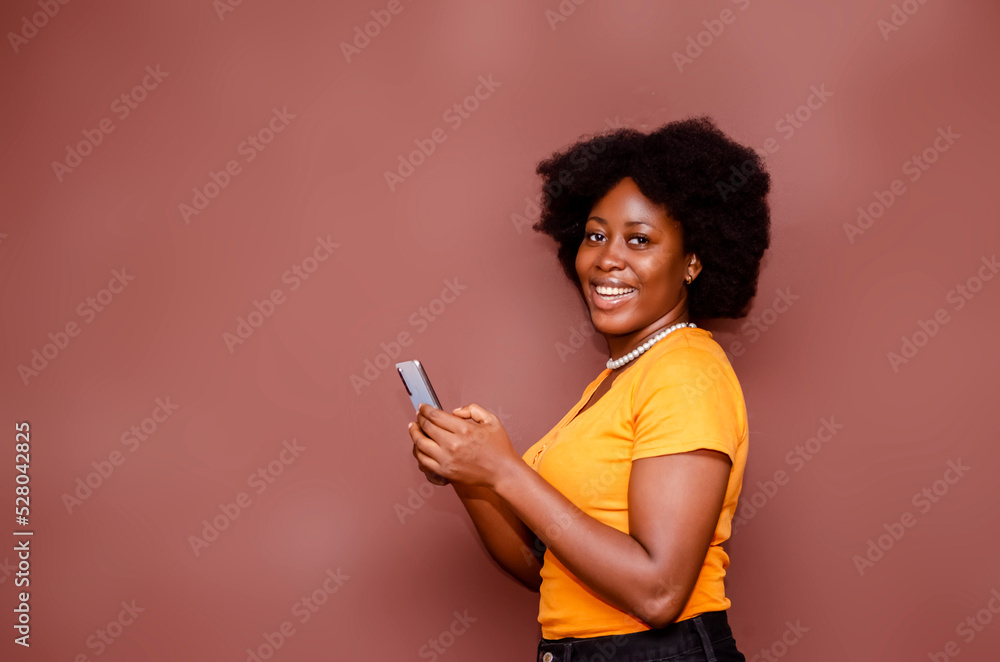 Happy excited African American lady on Afro hair style using mobile phone at studio standing behind a blank background Happy excited African American lady on Afro hair style using mobile phone at studio standing behind a blank background