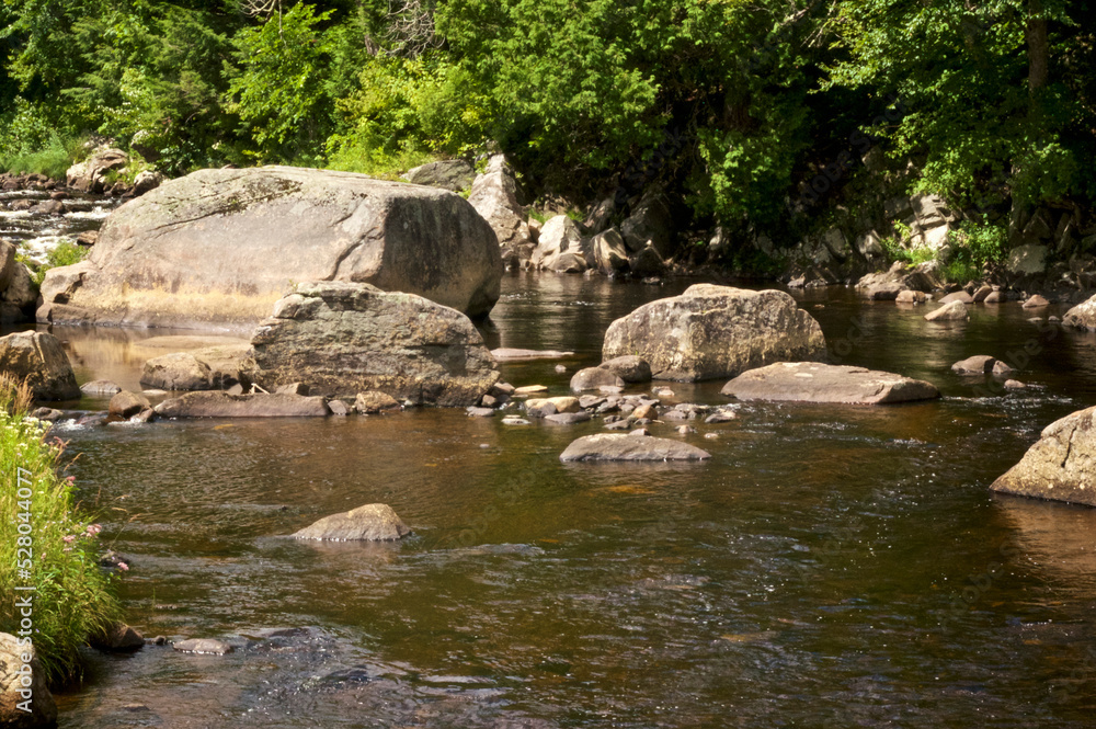 Large Rocks in the Au Sable River on a sunny summer afternoon, surrounded by trees and moving water, Lake Placid New York.