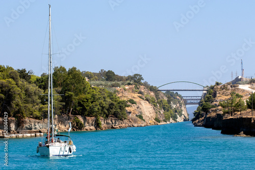 sailing boat passing Corinth Canal,  with the bridge on top connecting mainland Greece with Peloponnese. Isthmia, Corinthia, Peloponnese, Greece. Sunny day 
