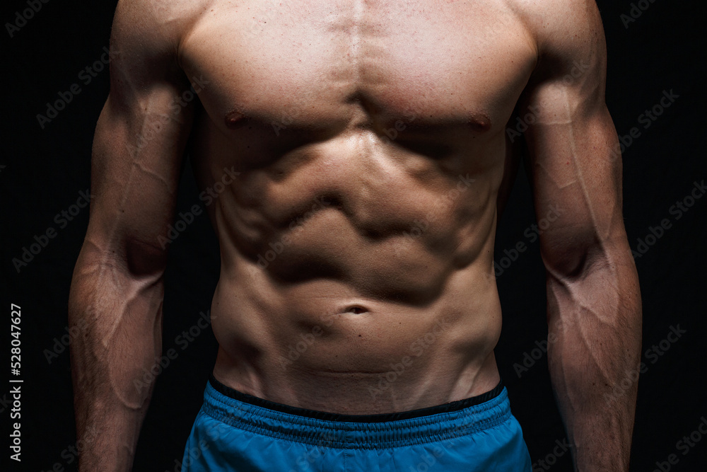 Well defined muscles due to working out to develop musculature in a strong  athletic man at his abdomen or belly, chest and arms showing great abs  Stock Photo