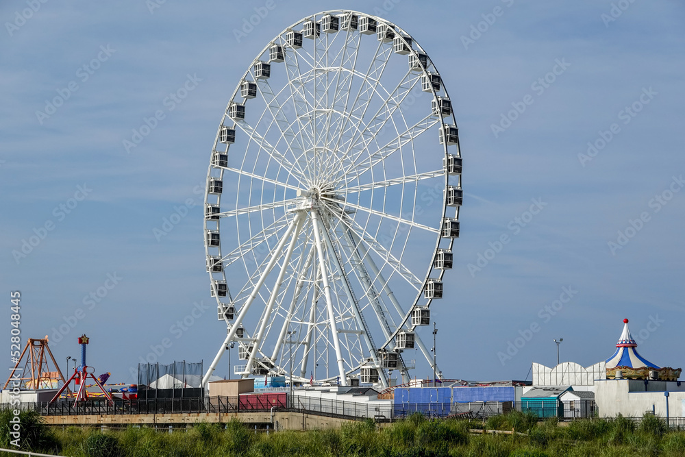 Tall ferris wheel and other amusements on a pier over the beach and near a wooden boardwalk