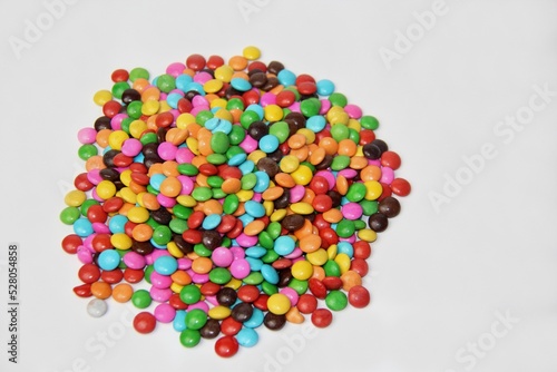 Colorful sugar covered chocolate candies stacked on a white background with space for text, selective focus, top view.