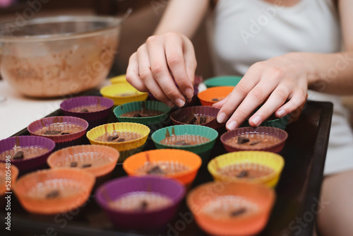 A young teenage girl makes homemade cupcakes at home, pours the dough into special rubber molds and puts chocolate, close up, focus on hands photo