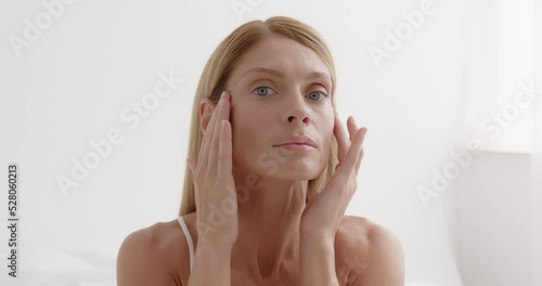 Closeup face of mature woman with wrinkles massaging face at home