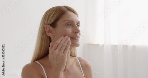 Woman applies anti aging cream on face undergoes beauty treatments cares about skin