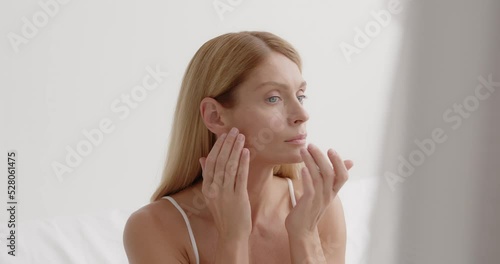 Gorgeous happy middle age woman looking at mirror touching her skin
